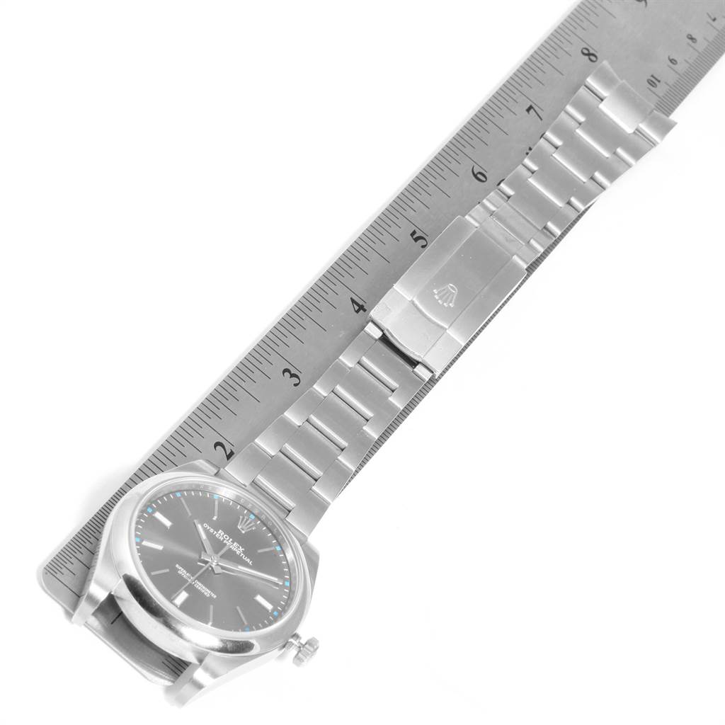 The image shows a side view of a Rolex Oyster Perpetual 114300 Men
s Stainless Steel Silver Dial 114300 Men
s Stainless Steel Silver Dial watch, highlighting its face, bracelet, and clasp next to a ruler.