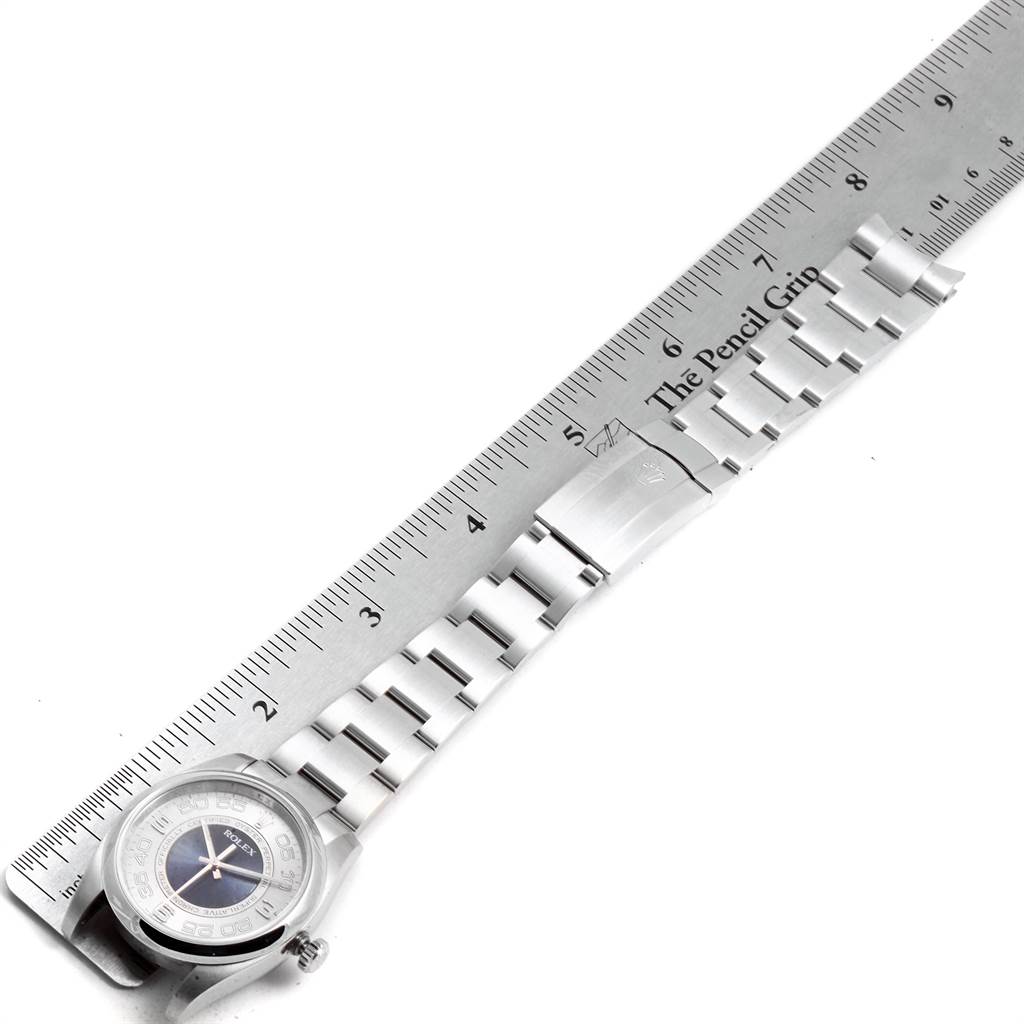 The Rolex Oyster Perpetual 116000 Men's Stainless Steel Silver Dial 116000 Men's Stainless Steel Silver Dial watch is shown flat, displaying its face, bracelet, and clasp alongside a ruler for scale.