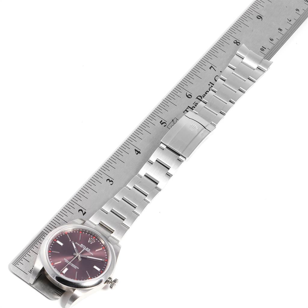 The image shows a Rolex Oyster Perpetual 114300 Men's Stainless Steel Burgundy Dial 114300 Men's Stainless Steel Burgundy Dial watch laid flat next to a ruler, displaying its face, bracelet, and clasp.