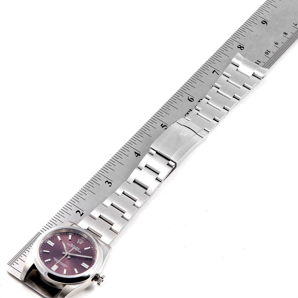 The image shows a top-down view of a Rolex Oyster Perpetual 116000 Men's Stainless Steel Burgundy Dial 116000 Men's Stainless Steel Burgundy Dial watch with its face, bracelet, and clasp laid beside a ruler.
