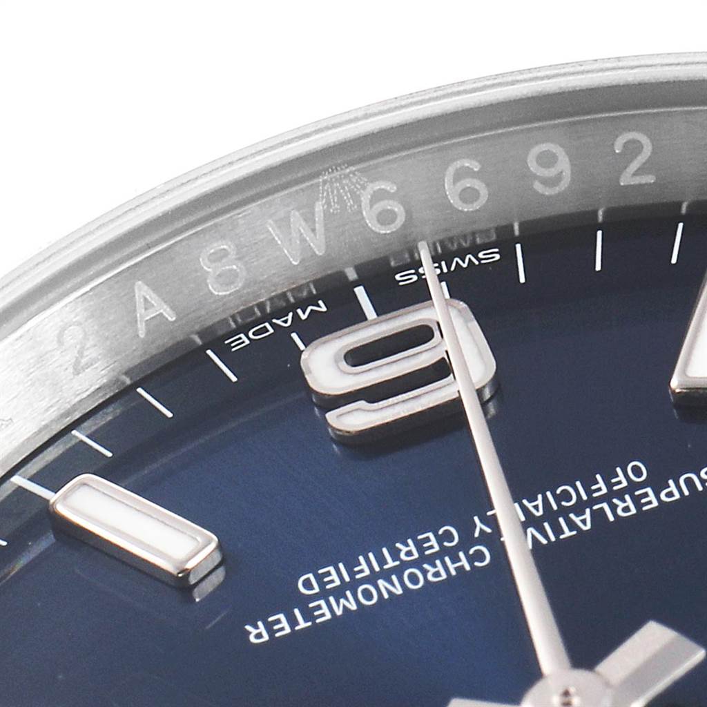 This close-up image of the Rolex Oyster Perpetual 116000 Men's Stainless Steel Blue Dial 116000 Men's Stainless Steel Blue Dial watch shows the dial, hours markers, part of the bezel, and serial number.