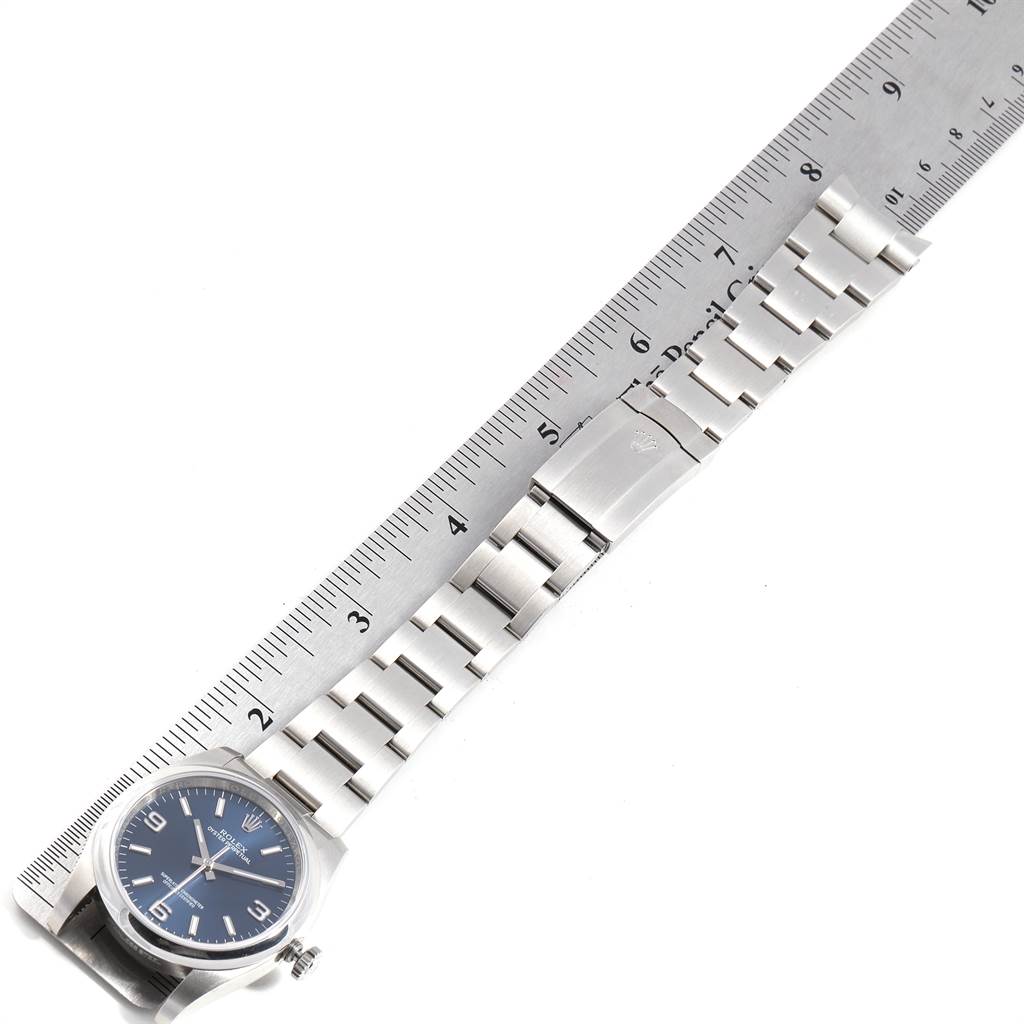 The image shows the Rolex Oyster Perpetual 116000 Men's Stainless Steel Blue Dial 116000 Men's Stainless Steel Blue Dial watch laid flat alongside a ruler, highlighting the bracelet and clasp.