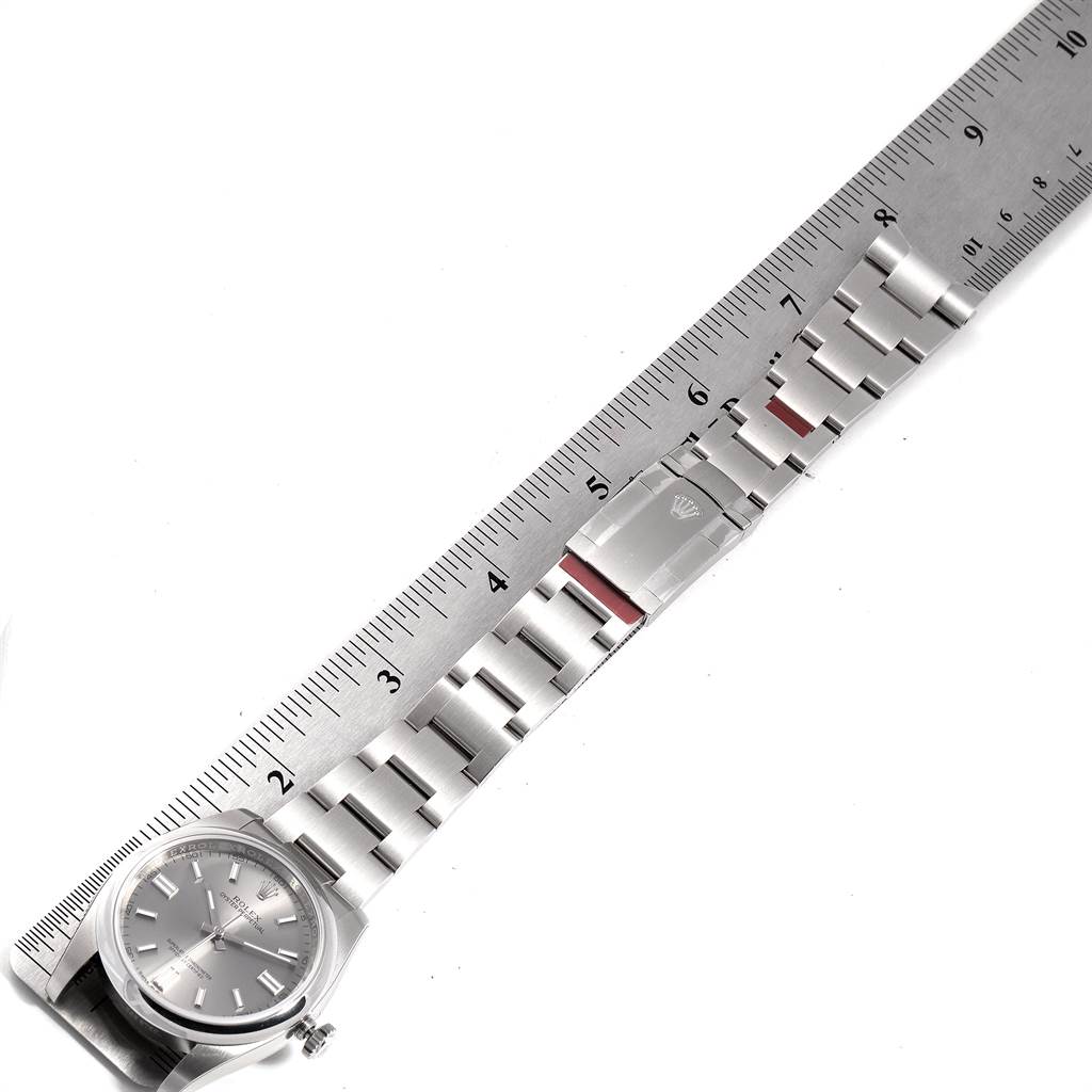 The image shows a top view of a Rolex Oyster Perpetual 116000 Men's Stainless Steel Grey Dial 116000 Men's Stainless Steel Grey Dial watch alongside a ruler, focusing on its dial, bracelet, and clasp.