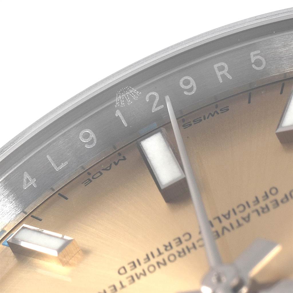 This close-up image of the Rolex Oyster Perpetual 114200 Men's Stainless Steel Champagne Dial 114200 Men's Stainless Steel Champagne Dial watch shows part of the face and hour markers, focusing on the 9, 12, and 5 markers.