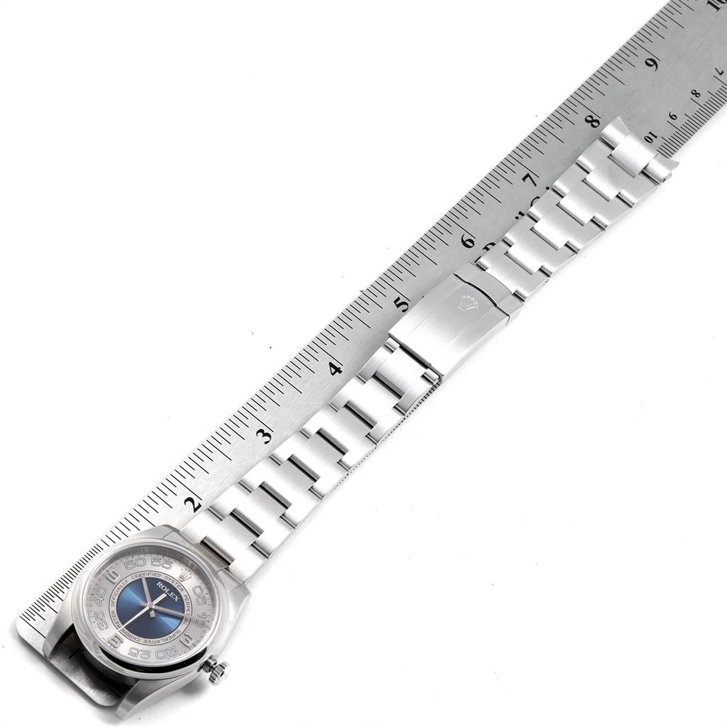 The image shows a Rolex Oyster Perpetual 116000 Men's Stainless Steel Silver Dial 116000 Men's Stainless Steel Silver Dial watch with a partially extended metal bracelet next to a ruler.