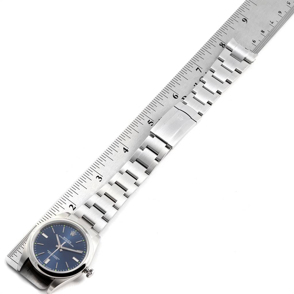 The image shows the full length of a Rolex Oyster Perpetual 114300 Men's Stainless Steel Blue Dial 114300 Men's Stainless Steel Blue Dial watch, including its stainless steel bracelet and clasp, alongside a ruler.