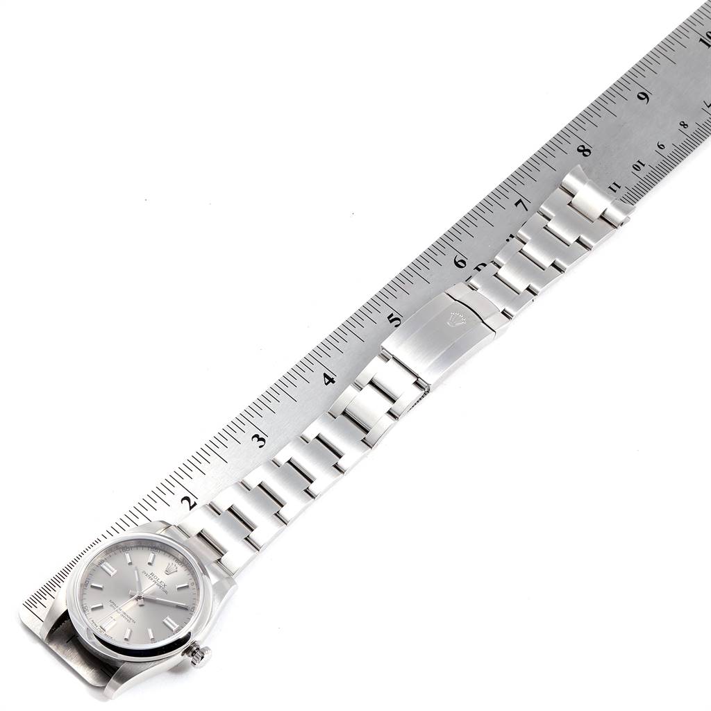 The image shows a flat-lay view of a Rolex Oyster Perpetual 116000 Men's Stainless Steel Grey Dial 116000 Men's Stainless Steel Grey Dial watch and its metal band beside a ruler.