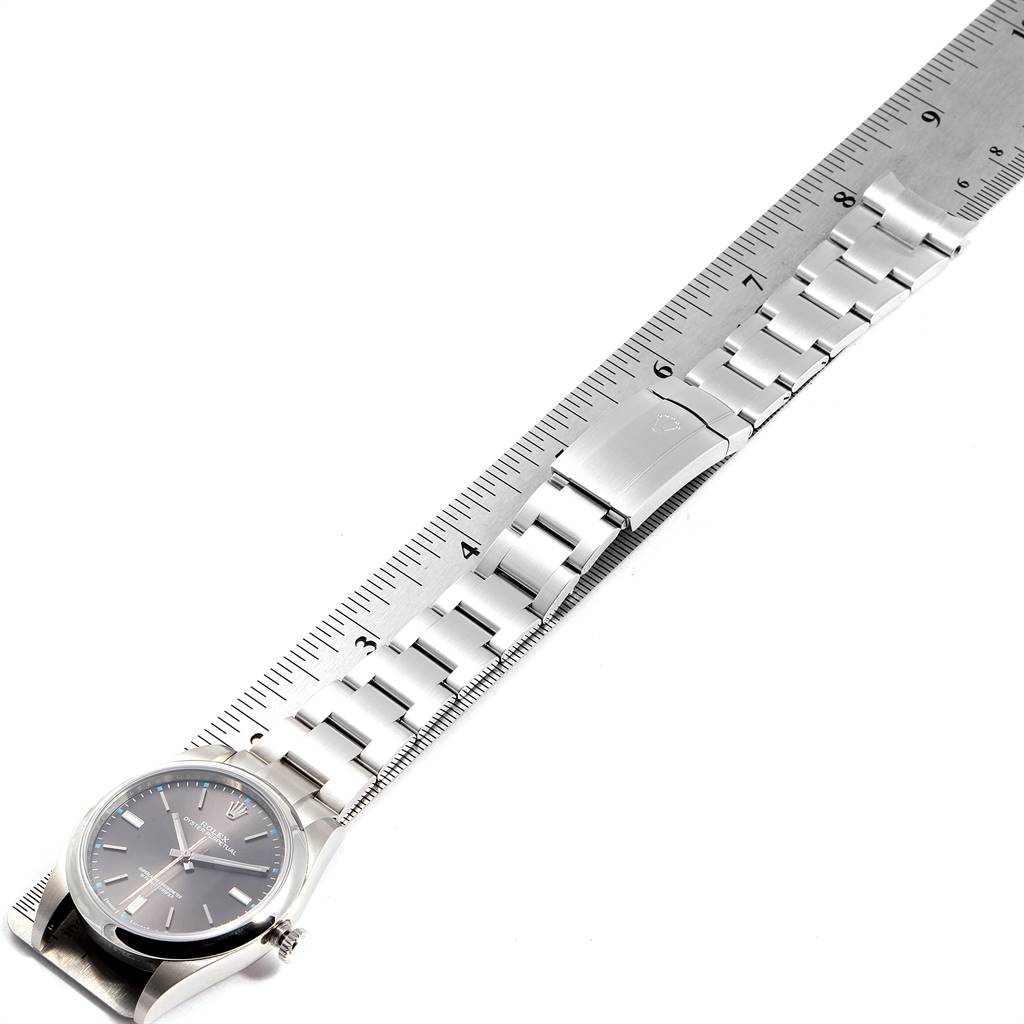 The image shows a Rolex Oyster Perpetual 114300 Men's Stainless Steel Silver Dial 114300 Men's Stainless Steel Silver Dial watch and its bracelet laid flat against a ruler, viewed from above.
