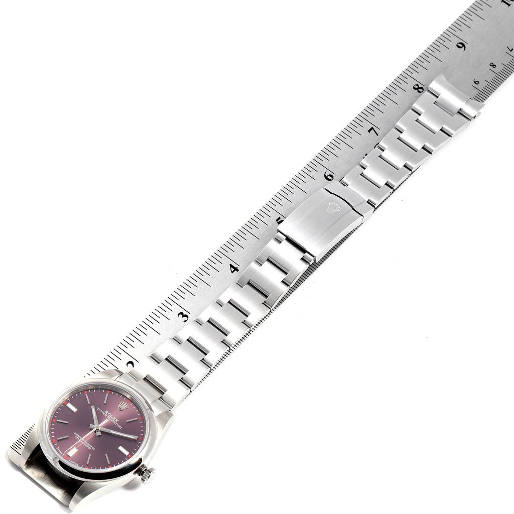 This image shows a top view of the Rolex Oyster Perpetual 114300 Men
s Stainless Steel Burgundy Dial 114300 Men
s Stainless Steel Burgundy Dial watch with a metal bracelet placed alongside a ruler.