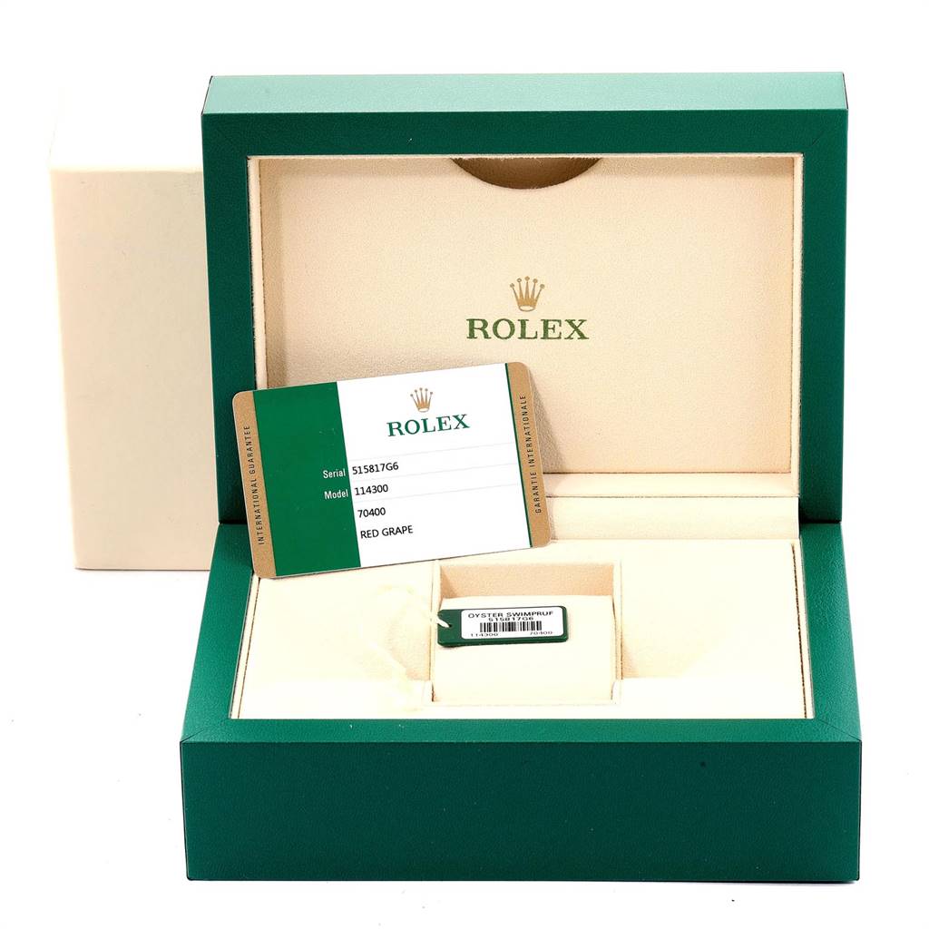 The image shows the open box and warranty card for a Rolex Oyster Perpetual 114300 Men
s Stainless Steel Burgundy Dial 114300 Men
s Stainless Steel Burgundy Dial model.