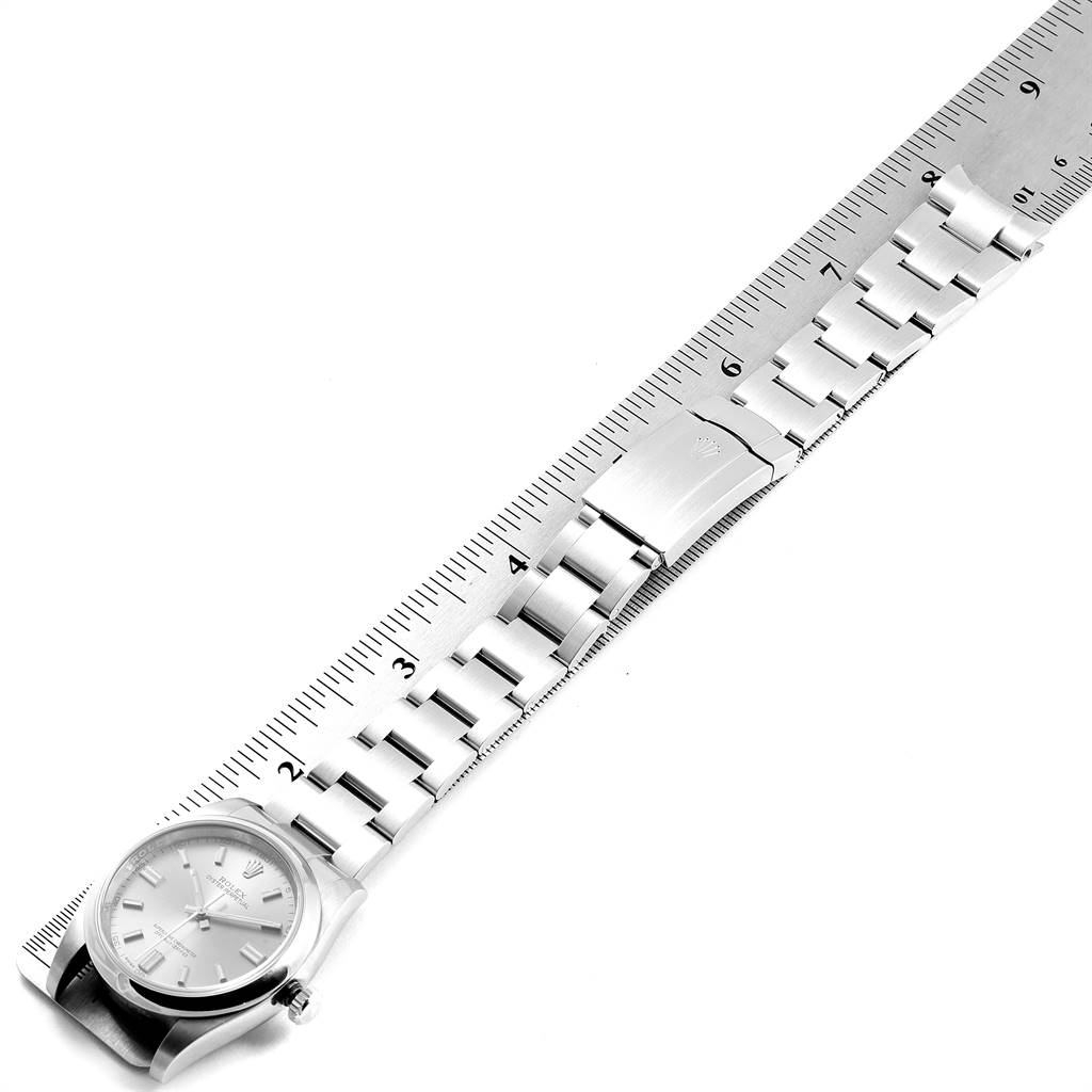 The Oyster Perpetual Rolex watch is shown diagonally with its entire bracelet and clasp next to a ruler for measurement.