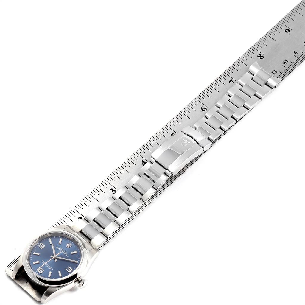 The image shows a Rolex Oyster Perpetual 116000 Men's Stainless Steel Blue Dial 116000 Men's Stainless Steel Blue Dial watch lying flat with its bracelet alongside a ruler for measurement.