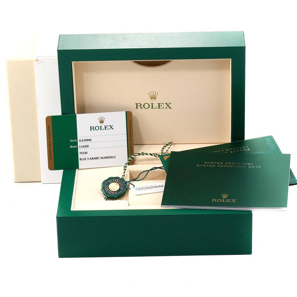 This image displays the box and accessories for a Rolex Oyster Perpetual 114200 Men's Stainless Steel Blue Dial 114200 Men's Stainless Steel Blue Dial model, including booklets, a tag, and a warranty card.