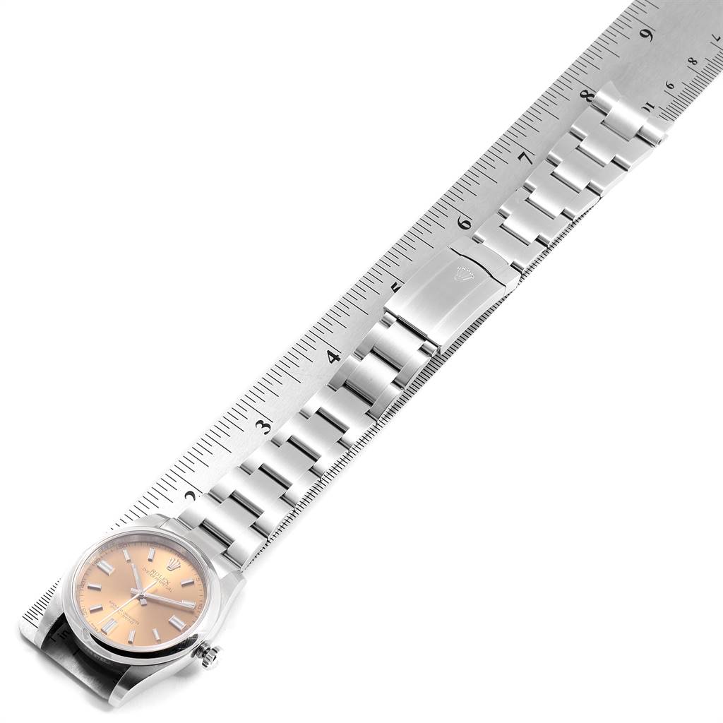 The image shows a Rolex Oyster Perpetual 116000 Men
s Stainless Steel Champagne Dial 116000 Men
s Stainless Steel Champagne Dial watch with a metal bracelet laid alongside a ruler for measurement.