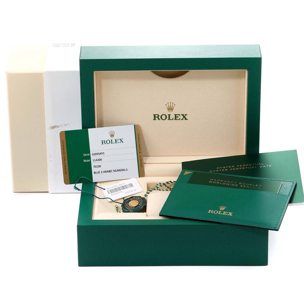 The image shows packaging and accessories for a Rolex Oyster Perpetual 114200 Men's Stainless Steel Blue Dial 114200 Men's Stainless Steel Blue Dial watch, including warranty cards and manual booklets.