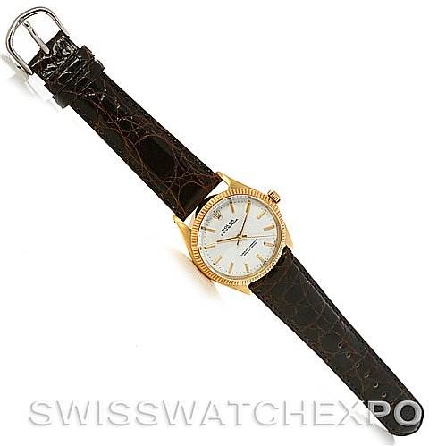 The image shows a top view of a Rolex Oyster Perpetual Men
s Yellow Gold White Dial Men
s Yellow Gold White Dial watch with a brown leather strap and a gold bezel.