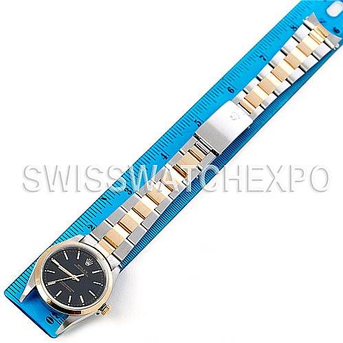 The Rolex Oyster Perpetual 14203 Men's Steel and Gold (two tone) Black Dial 14203 Men's Steel and Gold (two tone) Black Dial watch is shown laid flat on a blue ruler, highlighting its black dial and two-tone bracelet.