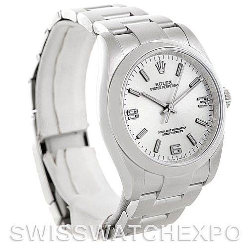 The Rolex Oyster Perpetual 116000 Men
s Stainless Steel Silver Dial 116000 Men
s Stainless Steel Silver Dial watch is shown at a left-side angle, displaying the face, case, bezel, and part of the bracelet.