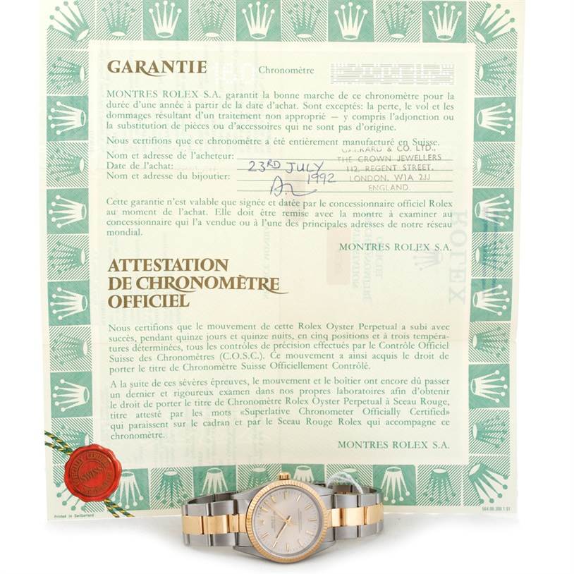 The image shows a Rolex Oyster Perpetual 14233 Men's Steel and Gold (two tone) Silver Dial 14233 Men's Steel and Gold (two tone) Silver Dial watch placed in front of its warranty and certification documents.