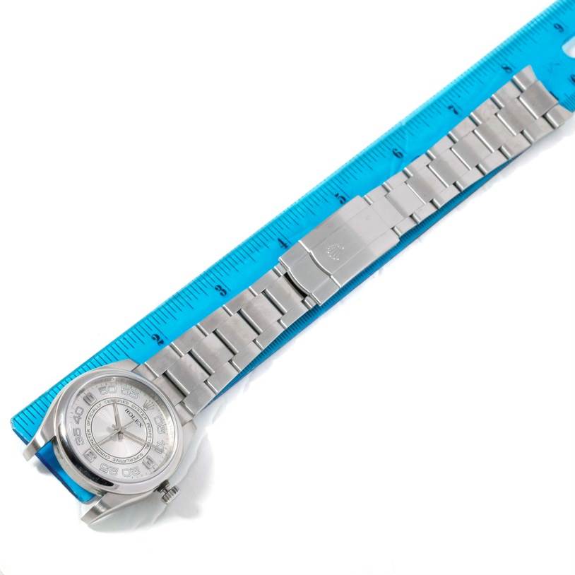 The image shows a top view of a Rolex Oyster Perpetual 116000 Men's Stainless Steel Silver Dial 116000 Men's Stainless Steel Silver Dial watch with a blue ruler measuring the length of the bracelet.