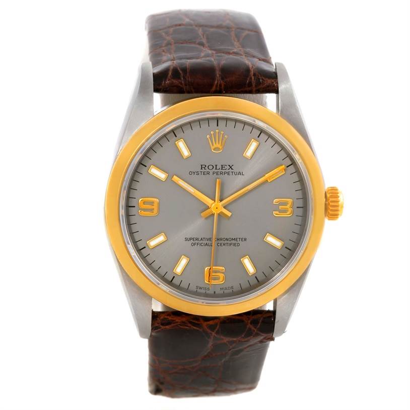 This image shows a front view of a Rolex Oyster Perpetual 14203 Men
s Steel and Gold (two tone) Grey Dial 14203 Men
s Steel and Gold (two tone) Grey Dial watch, featuring a gold bezel, brown leather strap, and silver dial with gold markers.