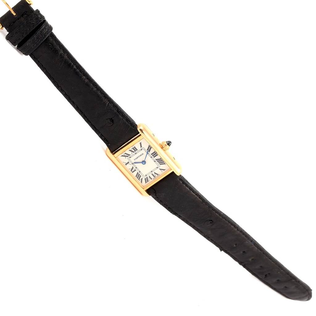 The Cartier Tank Louis W1529856 Women's Yellow Gold Silver Dial W1529856 Women's Yellow Gold Silver Dial watch is shown at an angle displaying its black leather strap and rectangular gold case with a white dial.