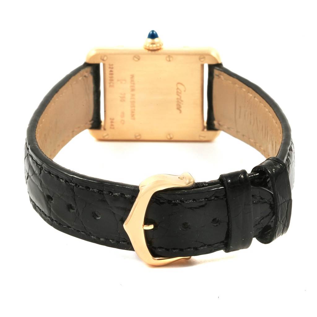 The image shows the back of a Tank Louis model by Cartier, highlighting its gold case, black leather strap, and clasp.