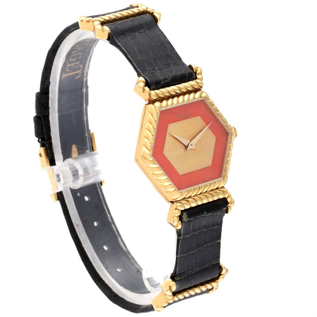The Piaget 9559 Women's Yellow Gold Pink Dial 9559 Women's Yellow Gold Pink Dial 9559 model watch is shown at an angle, displaying its hexagonal coral dial, gold case, and black strap.