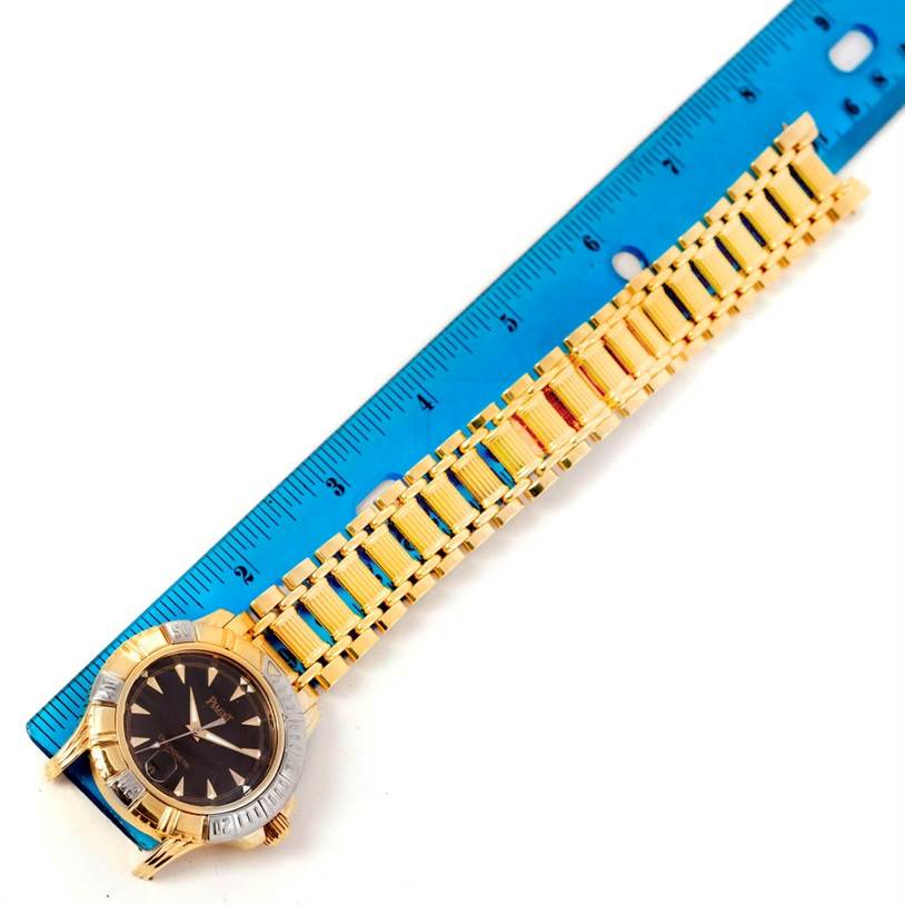 The Polo Key Dive 18K Yellow and White Gold Mens Watch 25020 by Piaget Men's Yellow Gold Black Dial Men's Yellow Gold Black Dial is shown from the top with its face and bracelet alongside a ruler.