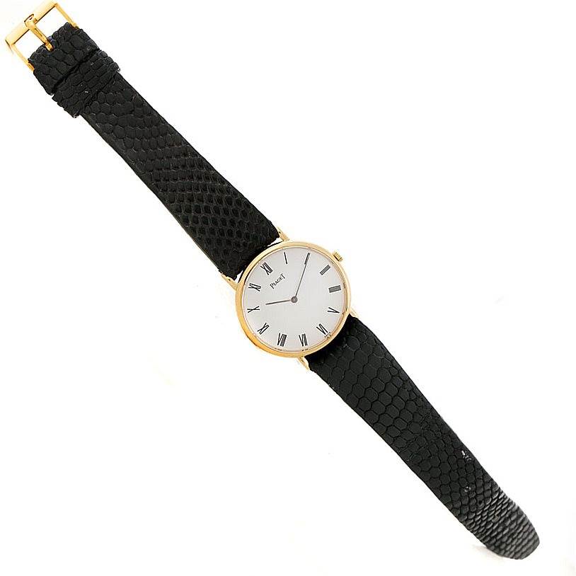 The image shows a Piaget 9025 Men's Yellow Gold White Dial 9025 Men's Yellow Gold White Dial 9025 18K yellow gold mechanical men's watch with a black textured strap from a top-down angle.