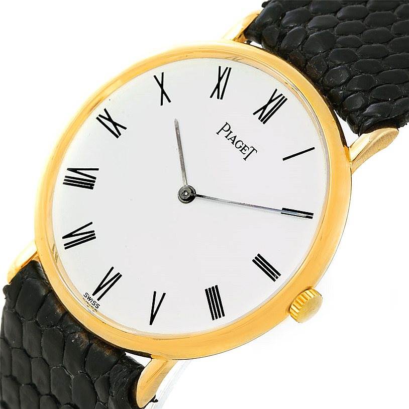 The image shows a close-up angle of the Piaget 9025 Men's Yellow Gold White Dial 9025 Men's Yellow Gold White Dial 9025 model watch, highlighting its 18K yellow gold case, white dial with Roman numerals, and black strap.