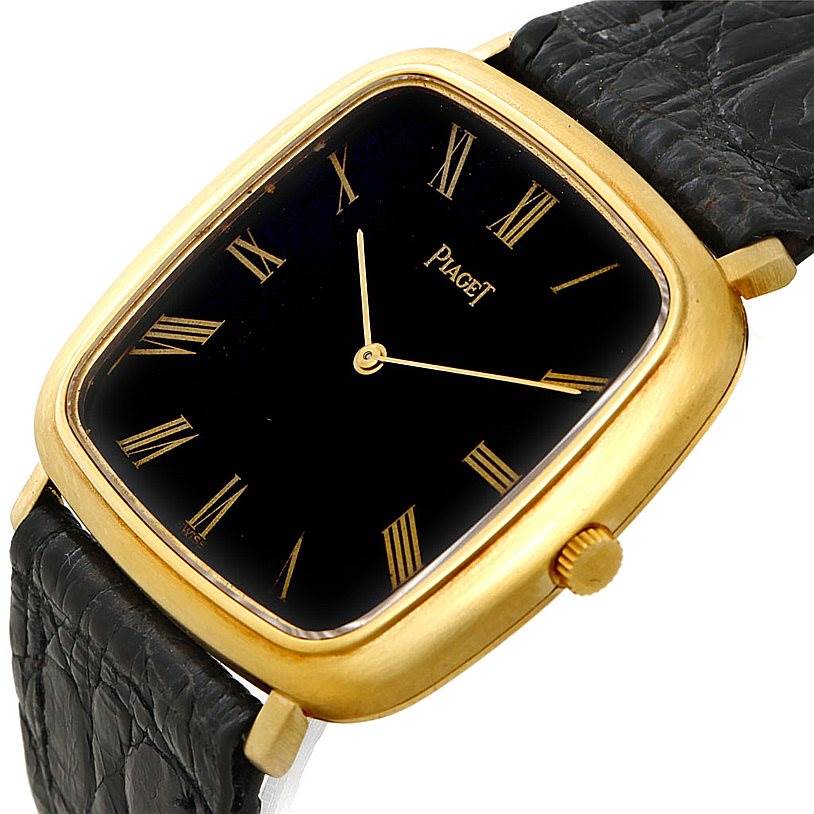 The image showcases a Piaget Men's Yellow Gold Black Dial Men's Yellow Gold Black Dial 18K Yellow Gold Cushion Shape Mechanical Mens Watch from an angled top-down view, highlighting the dial, bezel, and strap.
