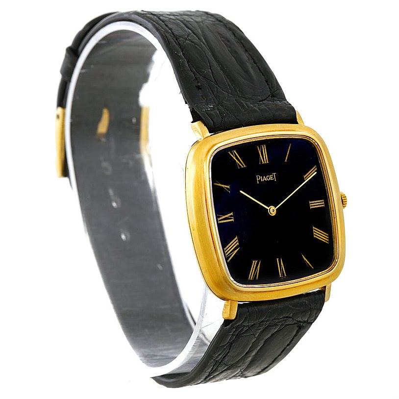 This image shows a Piaget Men's Yellow Gold Black Dial Men's Yellow Gold Black Dial 18K Yellow Gold Cushion Shape Mechanical Men's Watch from an angled side view, highlighting the black leather strap and gold case.