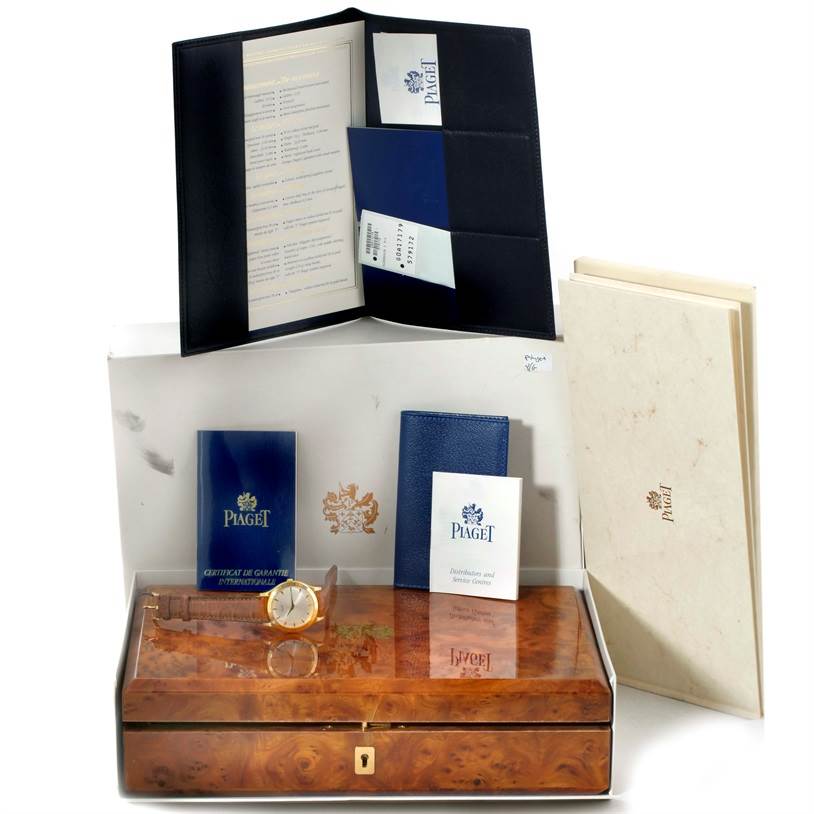 The image shows a Piaget 91000 Men's Yellow Gold Silver Dial 91000 Men's Yellow Gold Silver Dial 91000 model 18K Yellow Gold Mechanical Limited Edition Men's Watch with its box, papers, and booklets from a front angle.