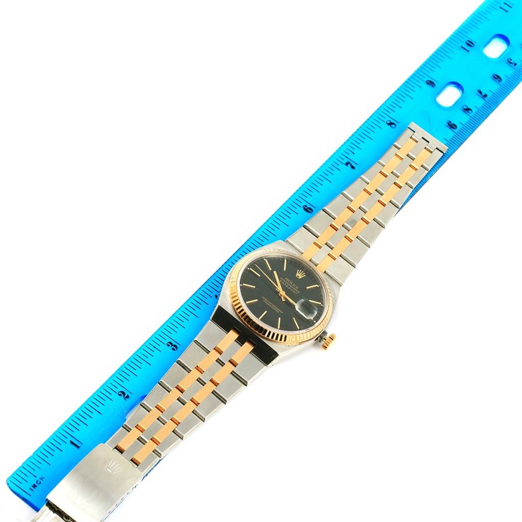 The Rolex Oysterquartz 17013 Men
s Stainless Steel Black Dial 17013 Men
s Stainless Steel Black Dial watch is shown flat with its face, bracelet, and clasp visible, and a blue ruler for size reference.