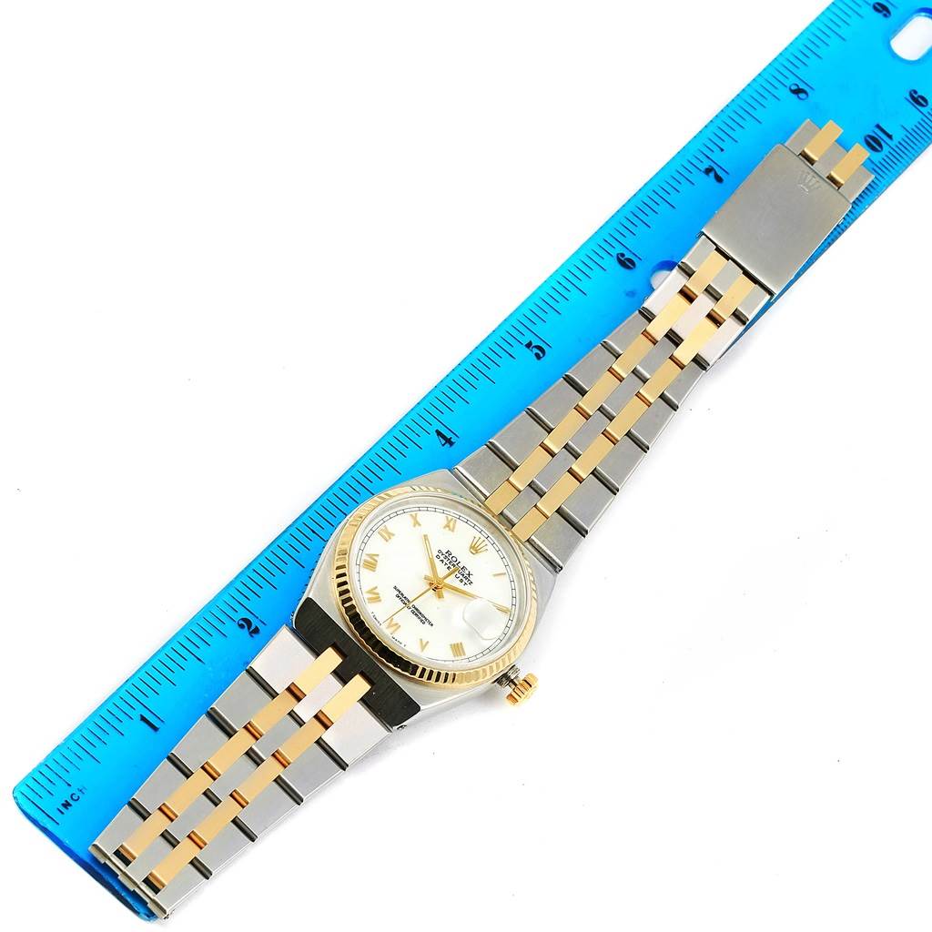 The Rolex Oysterquartz 17013 Men
s Stainless Steel White Dial 17013 Men
s Stainless Steel White Dial watch is displayed from a top-down angle alongside a blue ruler, showcasing its dial, bezel, and bracelet.