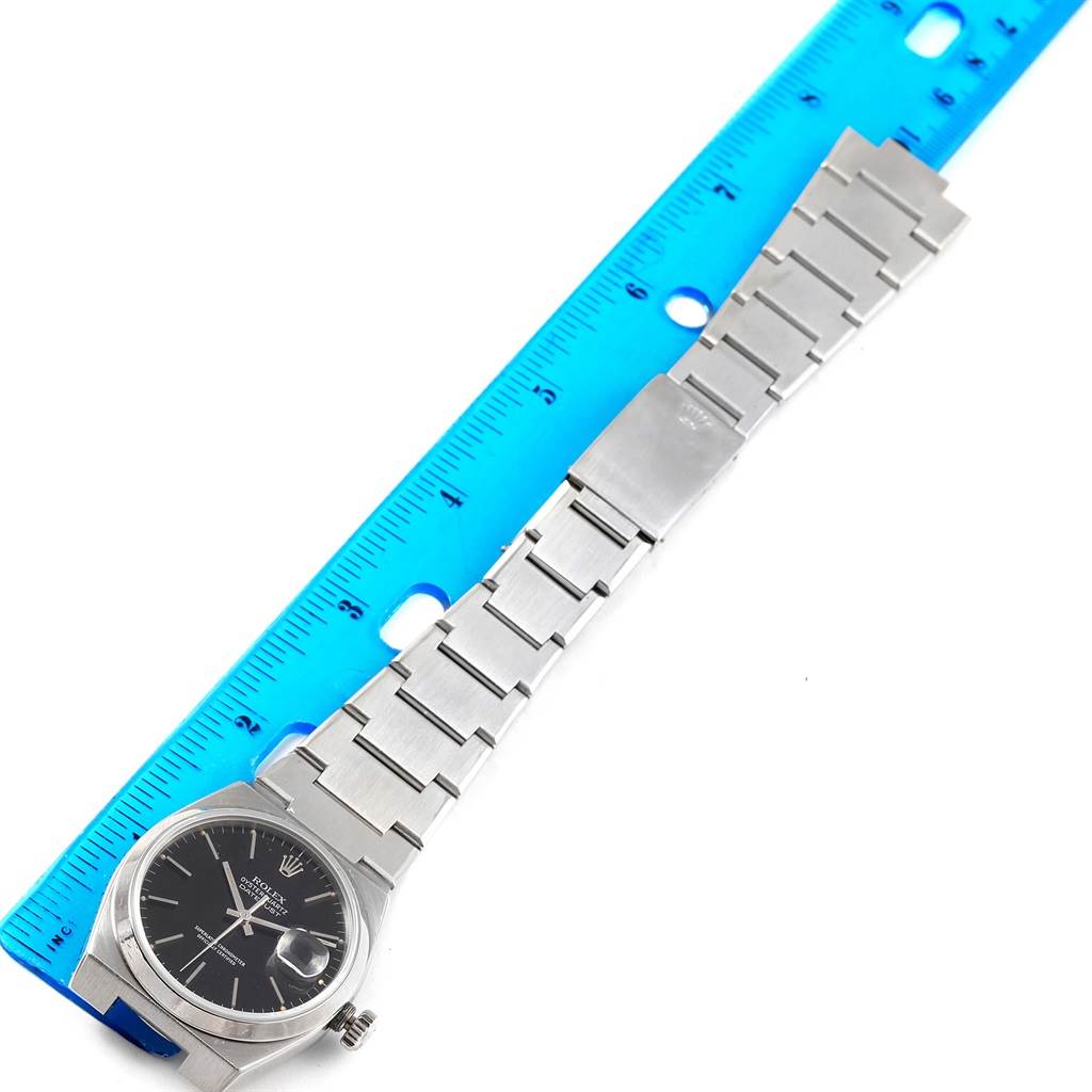 The image shows a top-down view of a Rolex Oysterquartz 17000 Men
s Stainless Steel Black Dial 17000 Men
s Stainless Steel Black Dial watch with a blue ruler measuring its bracelet.