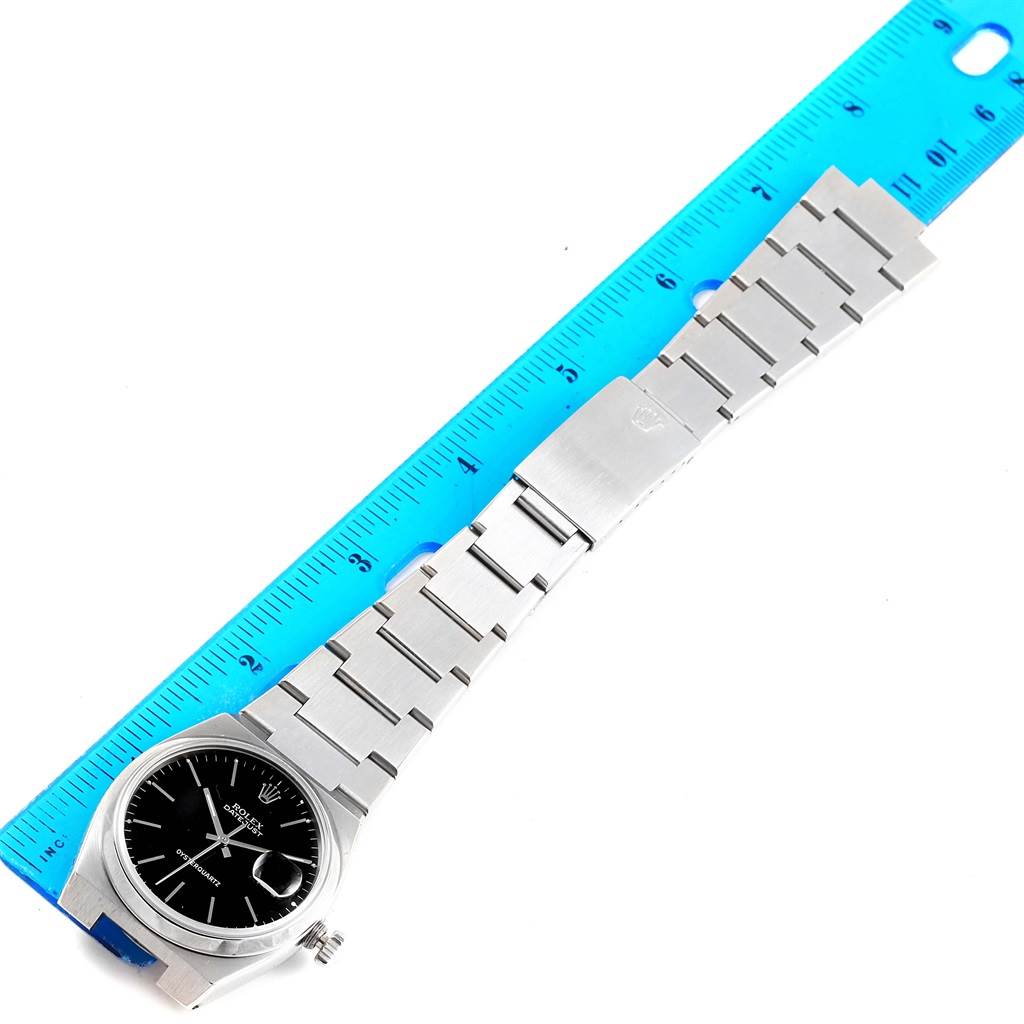 This image shows a top-down view of a Rolex Oysterquartz 17000 Men's Stainless Steel Black Dial 17000 Men's Stainless Steel Black Dial watch, displaying its face, strap, and clasp against a blue ruler.