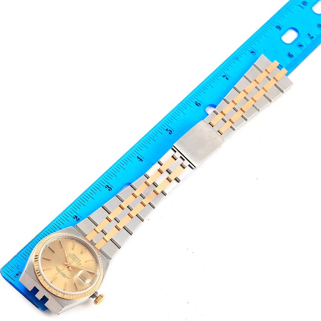 The image shows a Rolex Oysterquartz 17013 Men's Stainless Steel Champagne Dial 17013 Men's Stainless Steel Champagne Dial watch lying flat next to a blue ruler, displaying its face, crown, and two-tone bracelet.