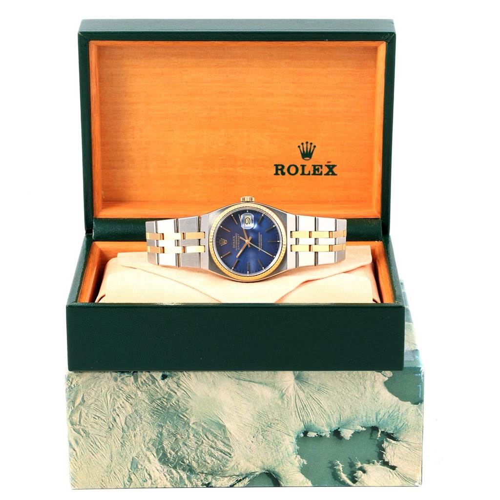 The Rolex Oysterquartz 17013 Men
s Stainless Steel Blue Dial 17013 Men
s Stainless Steel Blue Dial watch is shown from the front, displayed in an open green and tan box.