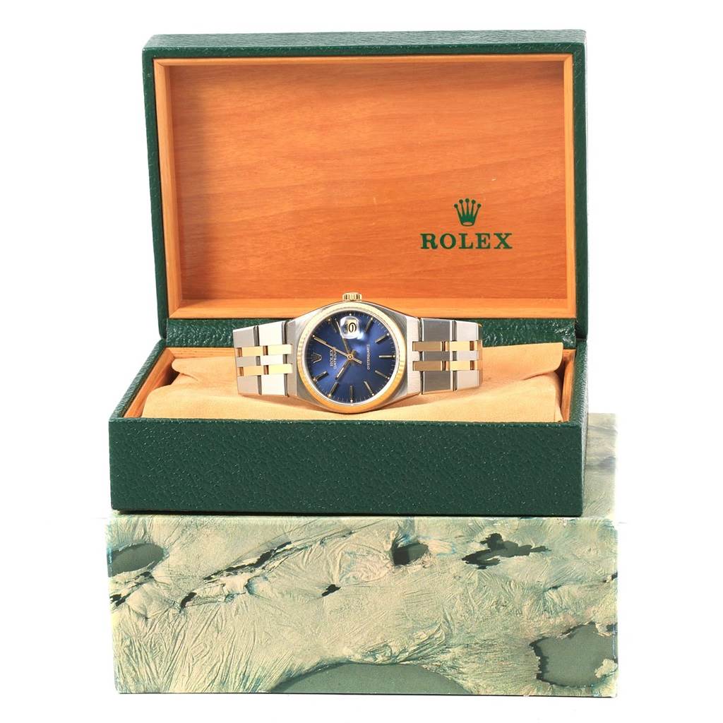 The Rolex Oysterquartz 17013 Men
s Steel and Gold (two tone) Blue Dial 17013 Men
s Steel and Gold (two tone) Blue Dial watch is displayed in its open green and wooden box, showing the face and bracelet.