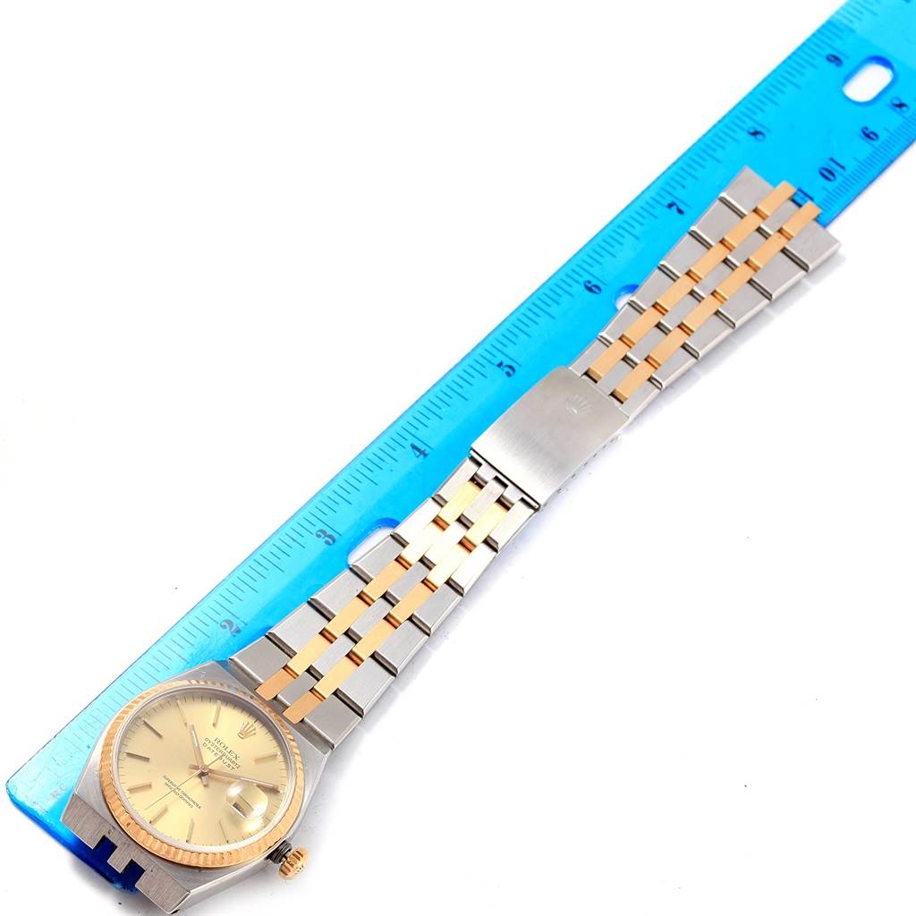 The Rolex Oysterquartz 17013 Men's Stainless Steel Champagne Dial 17013 Men's Stainless Steel Champagne Dial watch is shown from a top-down angle with its face, bezel, and part of the band visible next to a ruler.