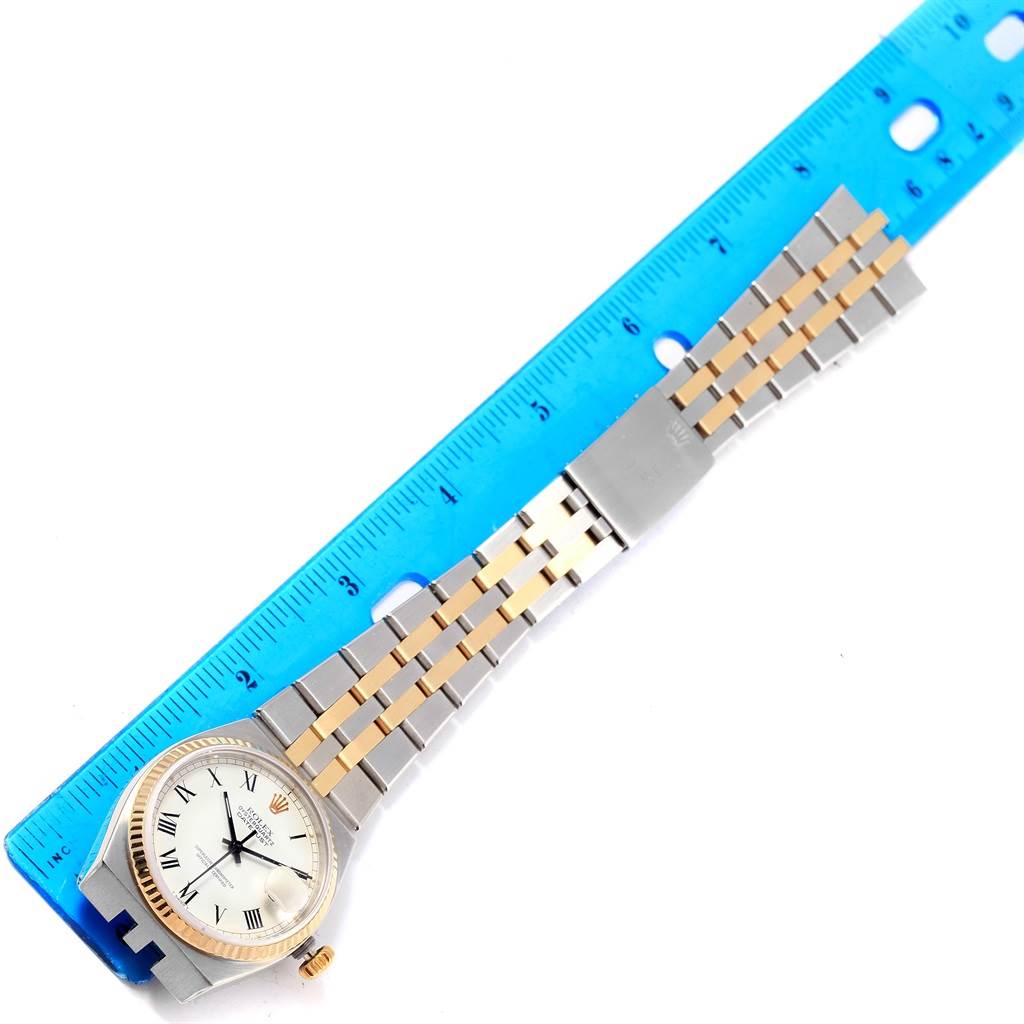 The image shows a Rolex Oysterquartz 17013 Men's Steel and Gold (two tone) White Dial 17013 Men's Steel and Gold (two tone) White Dial watch laid flat next to a blue ruler, displaying its face and bracelet.