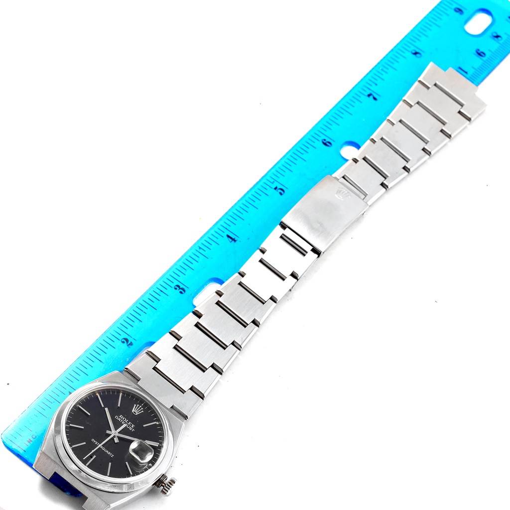 The image shows a Rolex Oysterquartz 17000 Men's Stainless Steel Black Dial 17000 Men's Stainless Steel Black Dial watch laid flat next to a blue ruler, displaying its full face, metal bracelet, and clasp.