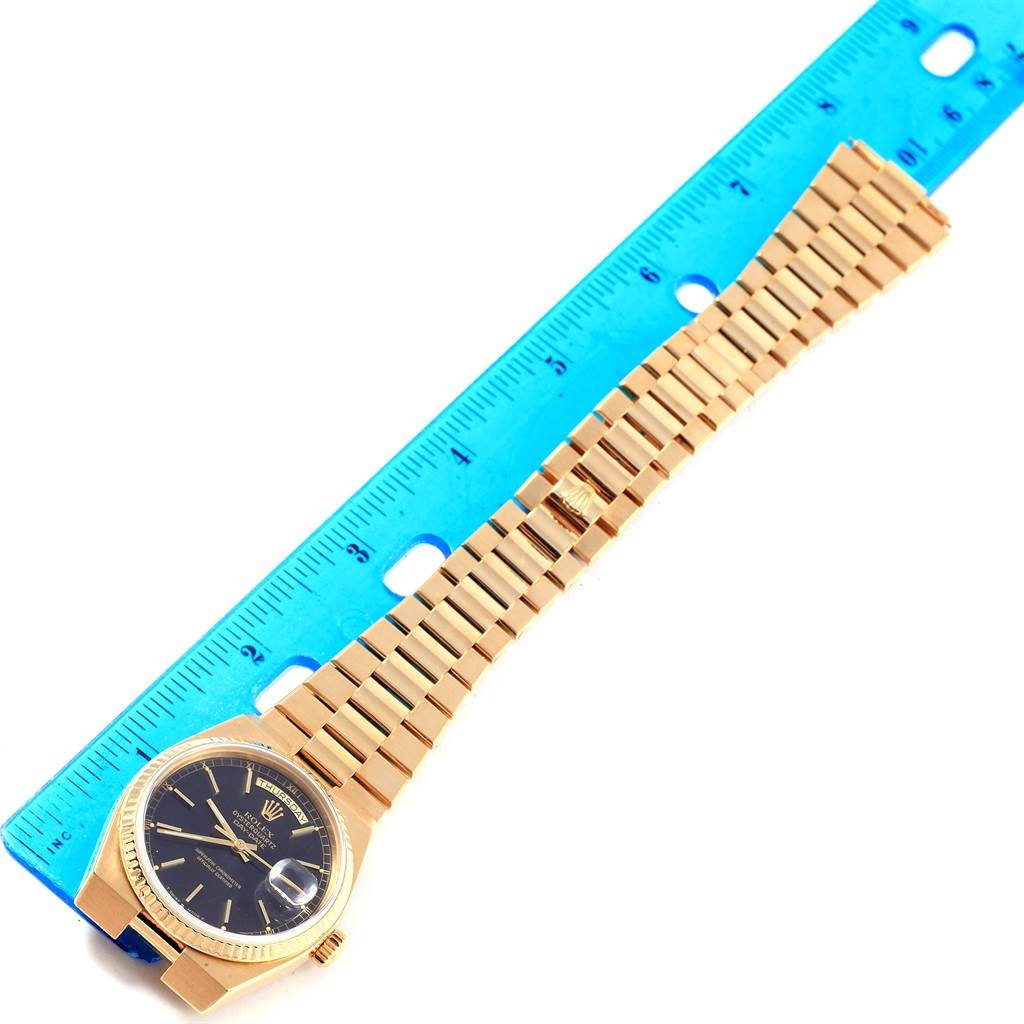 The image shows a Rolex Oysterquartz 19018 Men
s Yellow Gold Black Dial 19018 Men
s Yellow Gold Black Dial watch placed at an angle next to a blue ruler, displaying the watch face and full bracelet.