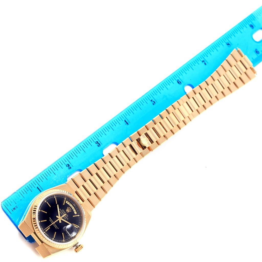 A Rolex Oysterquartz 19018 Men's Yellow Gold Black Dial 19018 Men's Yellow Gold Black Dial watch is shown laid flat beside a blue ruler, displaying its gold bracelet and black dial.