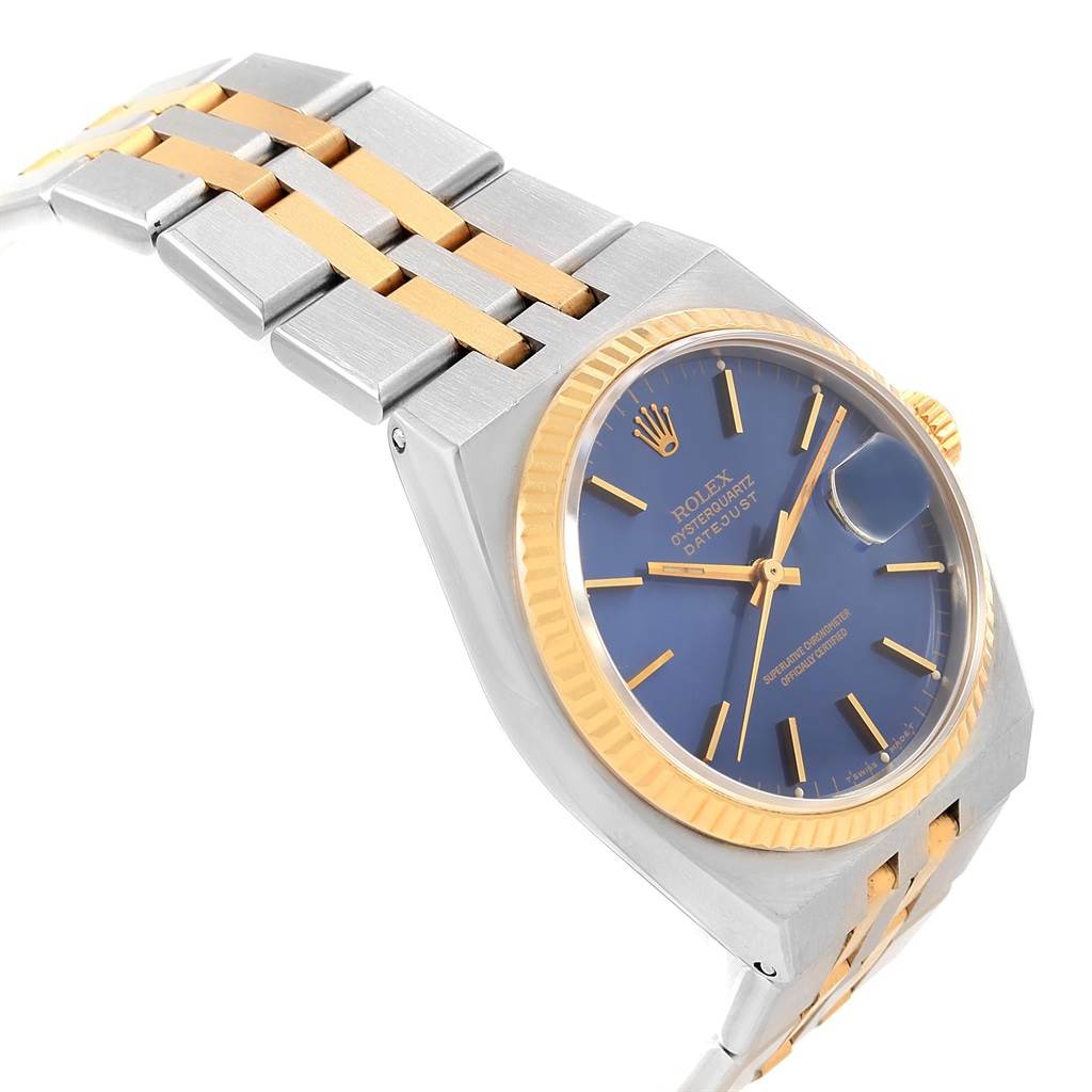 The image shows a side angle of a Rolex Oysterquartz 17013 Men
s Stainless Steel Blue Dial 17013 Men
s Stainless Steel Blue Dial watch, highlighting its blue dial, gold bezel, and two-tone metal bracelet.