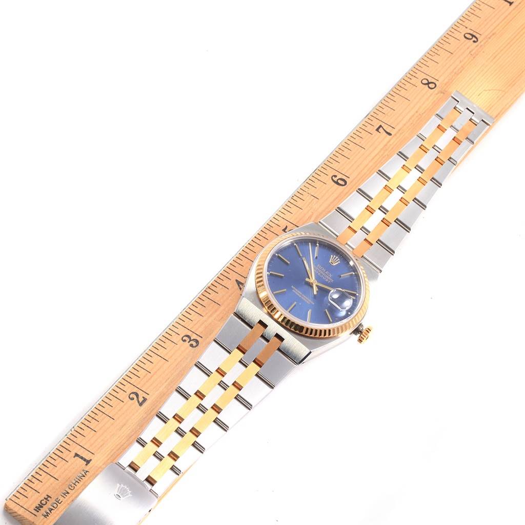 The image shows a top view of a Rolex Oysterquartz 17013 Men's Stainless Steel Blue Dial 17013 Men's Stainless Steel Blue Dial watch with a blue dial, two-tone bracelet, and a ruler for scale.