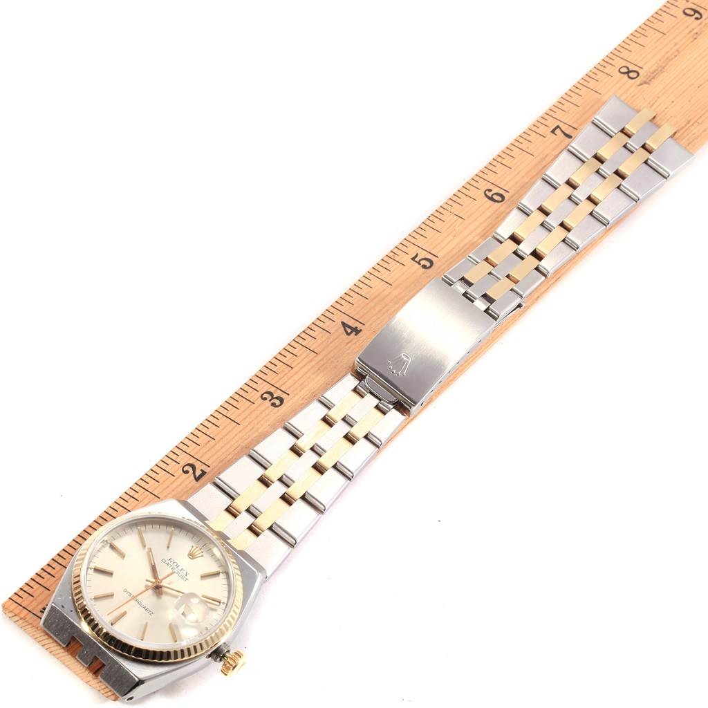 The Rolex Oysterquartz 17013 Men's Stainless Steel Silver Dial 17013 Men's Stainless Steel Silver Dial watch is laid flat next to a ruler, showing the face, band, and clasp at an overhead angle.