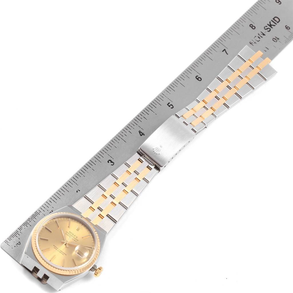 The Rolex Oysterquartz 17013 Men
s Stainless Steel Champagne Dial 17013 Men
s Stainless Steel Champagne Dial watch is shown from a top-down angle, displaying its face, bracelet, and clasp, alongside a ruler for measurement.